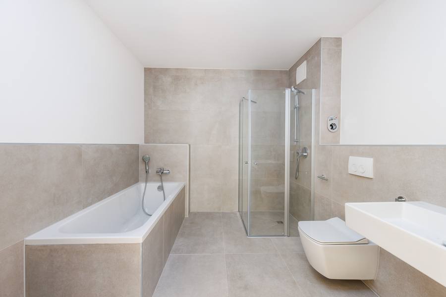 Bad mit großformatigen hellen Fliesen, Badewanne und Glasdusche